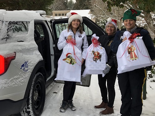 Three people holding Christmas hampers in front of a police car