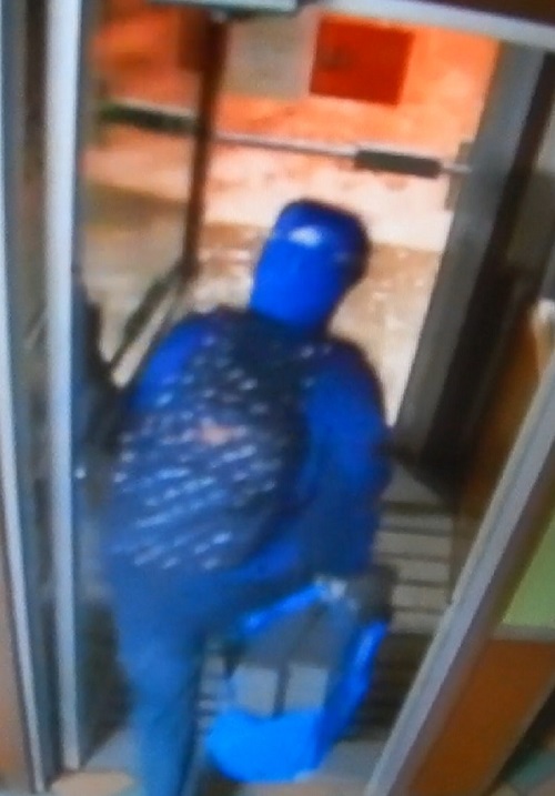 Suspect wearing a blue winter coat, blue backpack, carrying two stolen cash registers in a blue bag
