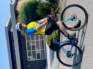 Cpl. Tarmii Miskiw in cycling gear on a blue bicycle in front of a house