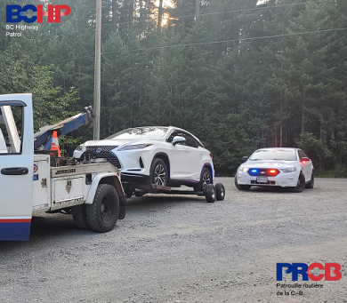 Side view of white Lexus SUV hooked up behind tow truck, with a police car behind it