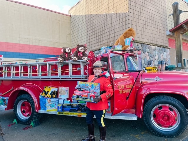 A vintage fire truck filled with toys and a RCMP officer in red serge holding toys